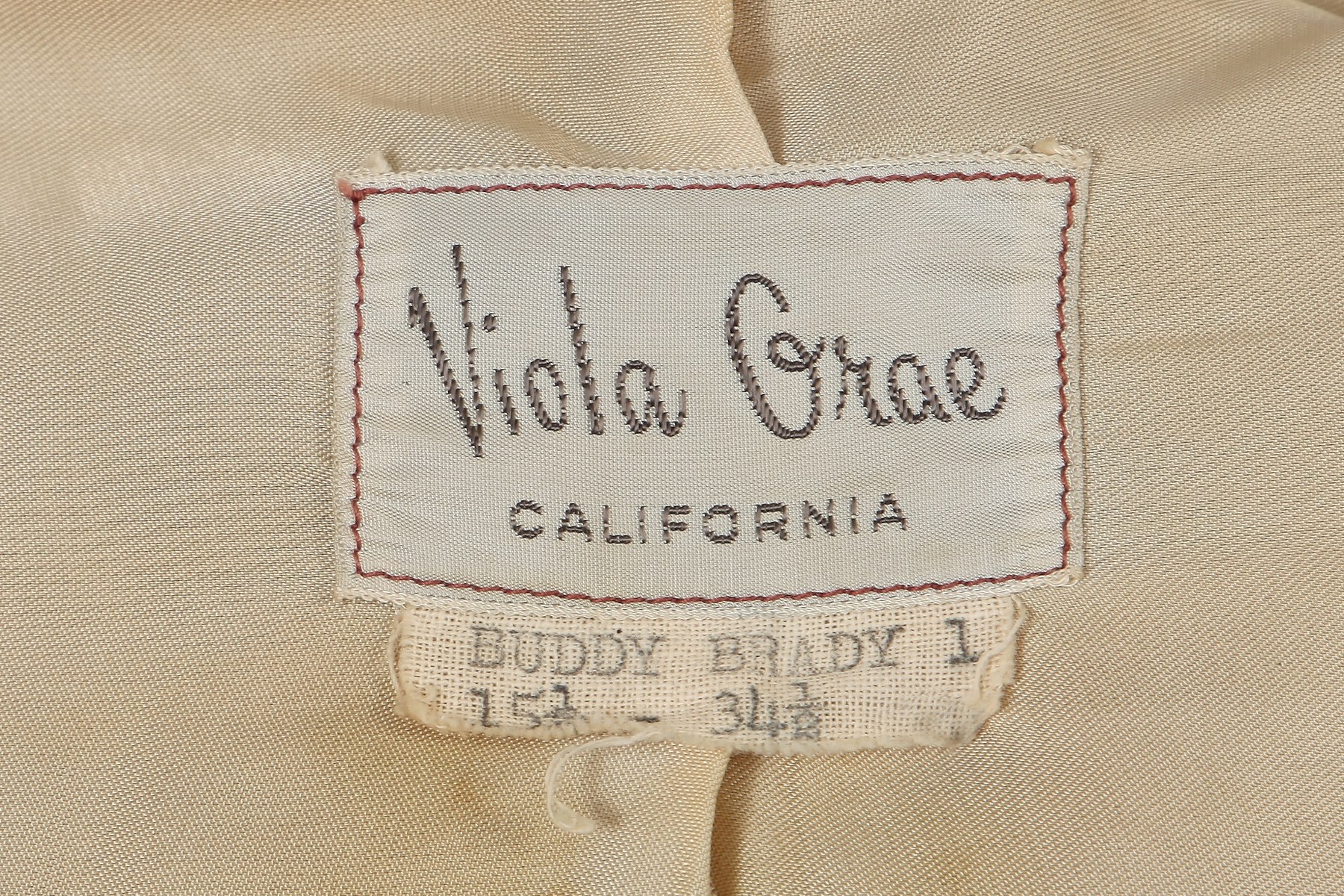 The shirt carries a “Viola Grae / California” label above another reading “Buddy Brady 1”; the latter is a named lead, not a confirmed wearer identification.