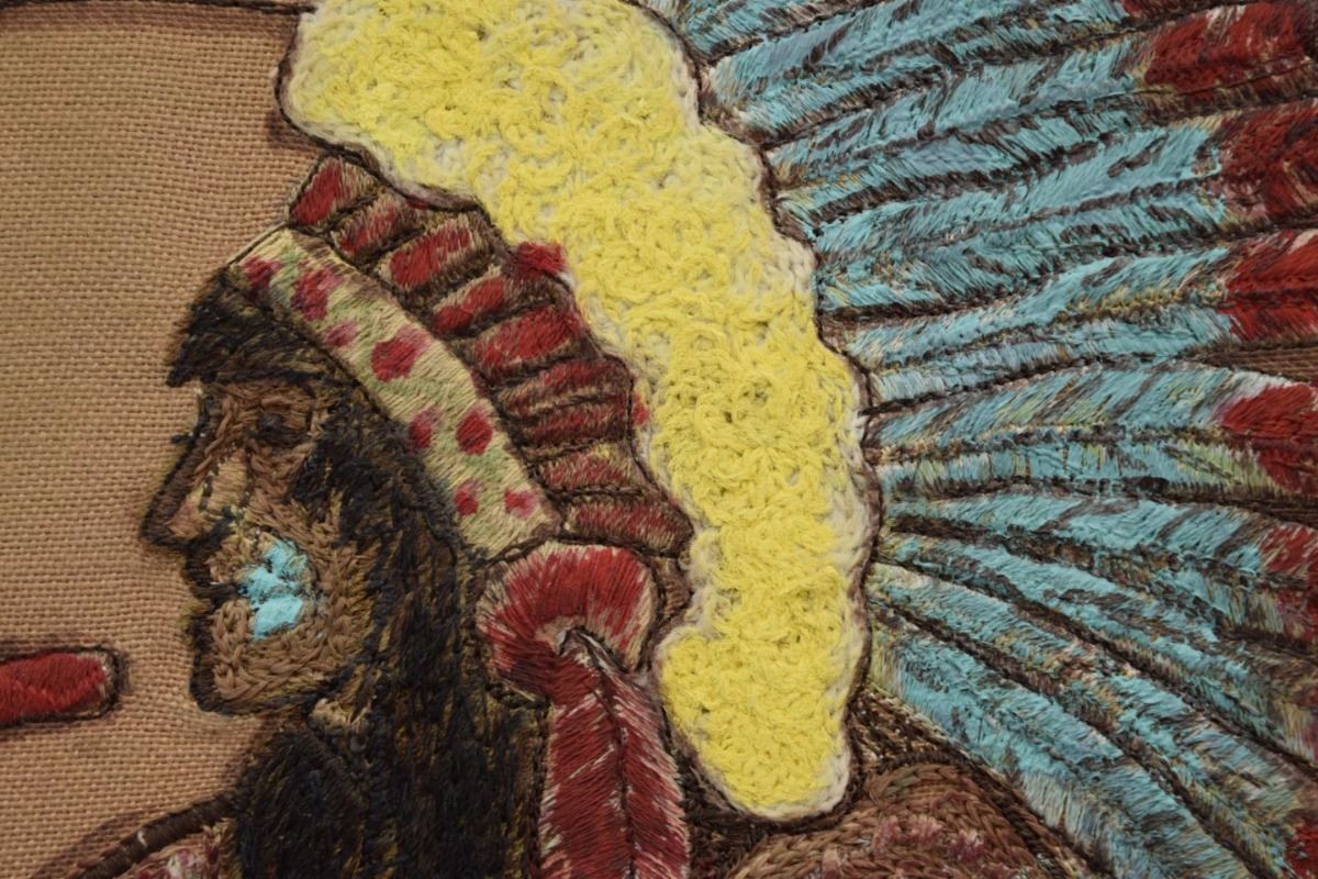 Close view of the needlepoint’s figure and feathered headdress, as photographed for the auction presentation.