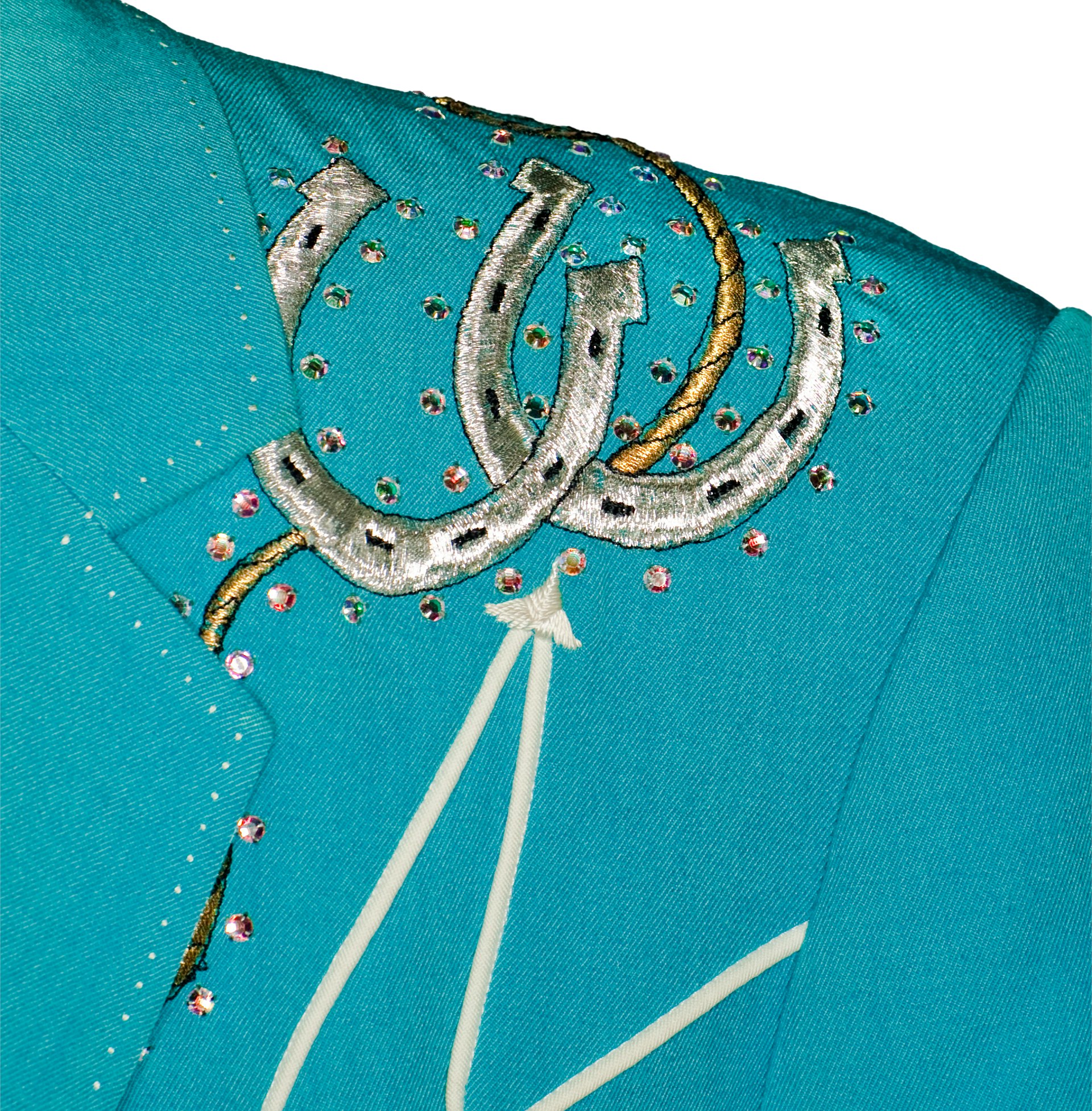 Close exhibition view of Dwight Yoakam’s Manuel-designed Hillbilly Deluxe bolero, showing its turquoise ground, silver horseshoe, rhinestones, piping and arrowhead detail.